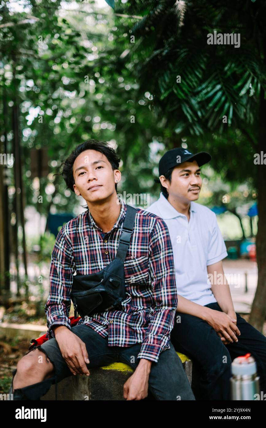 Deux hommes d'Asie du Sud-est assis sur une place de la ville, capturant un moment de détente et de conversation. Idéal pour les projets axés sur la vie urbaine, communi Banque D'Images