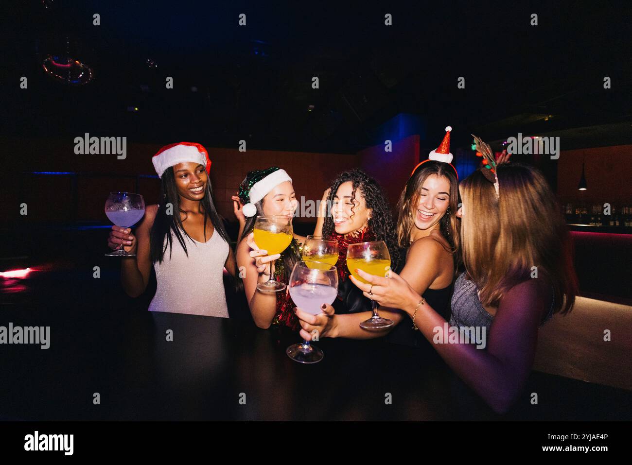 Un groupe d'amis célèbrent joyeusement la saison des fêtes avec des boissons dans une boîte de nuit, portant des chapeaux de Père Noël festifs et souriant. Banque D'Images