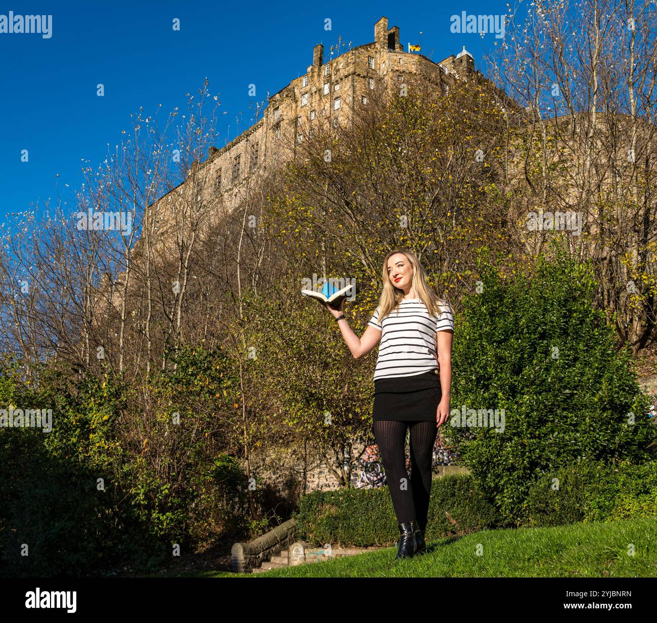 Édimbourg, Écosse, Royaume-Uni, 14 novembre 2024, Push the Boat Out : la chanteuse folklorique primée Iona Fyfe pose avec un bateau en papier origami sous l’emblématique château d’Édimbourg pour promouvoir le festival national de poésie écossais. Iona sera la tête d'affiche d'une soirée de chansons fusionnées de poésie. Crédit : Sally Anderson/Alamy Live News Banque D'Images