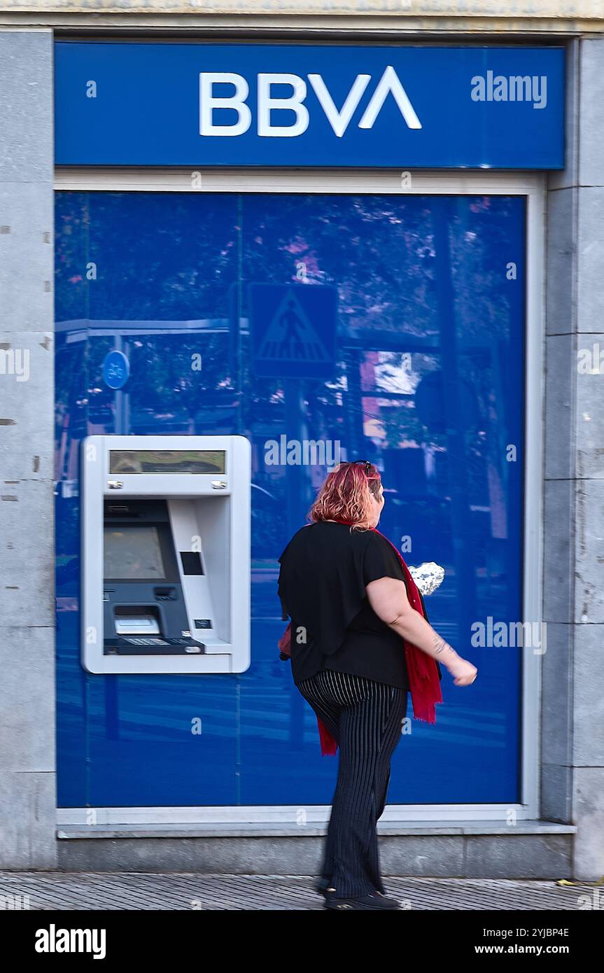 Viladecans. Espagne - 14 novembre 2024 : succursale bancaire BBVA avec une femme de passage, soulignant l'interaction entre la banque et ses clients. Le b Banque D'Images