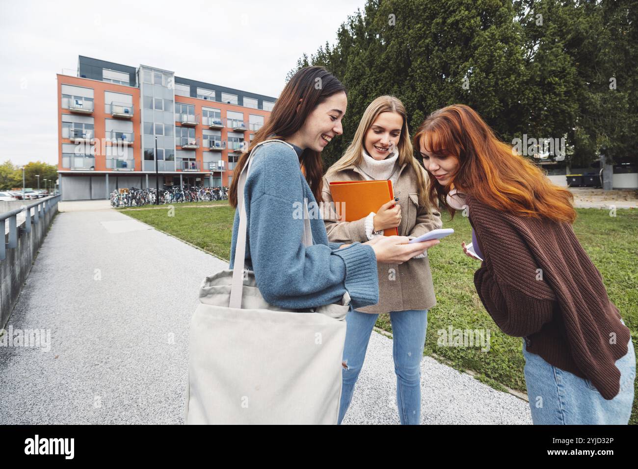 Groupe de trois étudiantes de collage joyeuses devant leur dortoir par un froid jour d'automne, marchant sur le campus pour se rendre à leur classe Banque D'Images