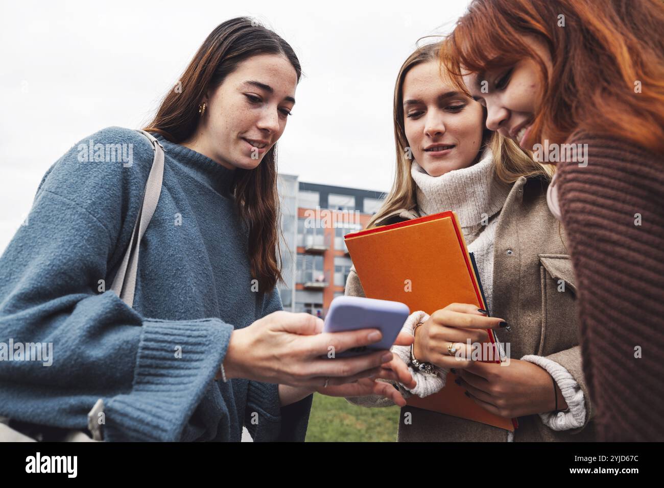 Groupe de trois étudiantes de collage joyeuses devant leur dortoir par un froid jour d'automne, marchant sur le campus pour se rendre à leur classe Banque D'Images