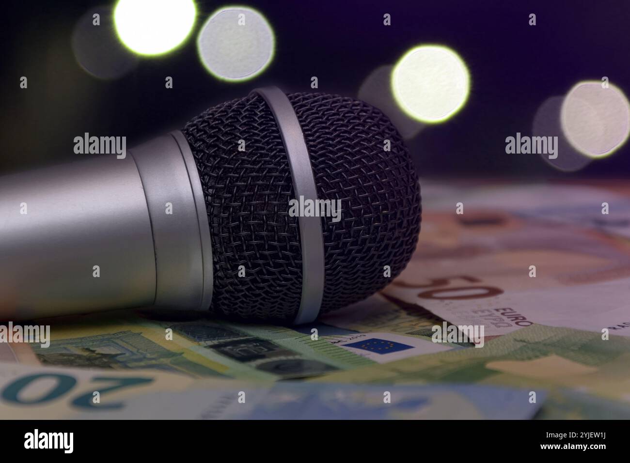 Le microphone repose sur une pile de billets en euros sur un fond de bokeh flou et de lumières. Concept : club de karaoké, frais d'artiste, paiement pour per Banque D'Images