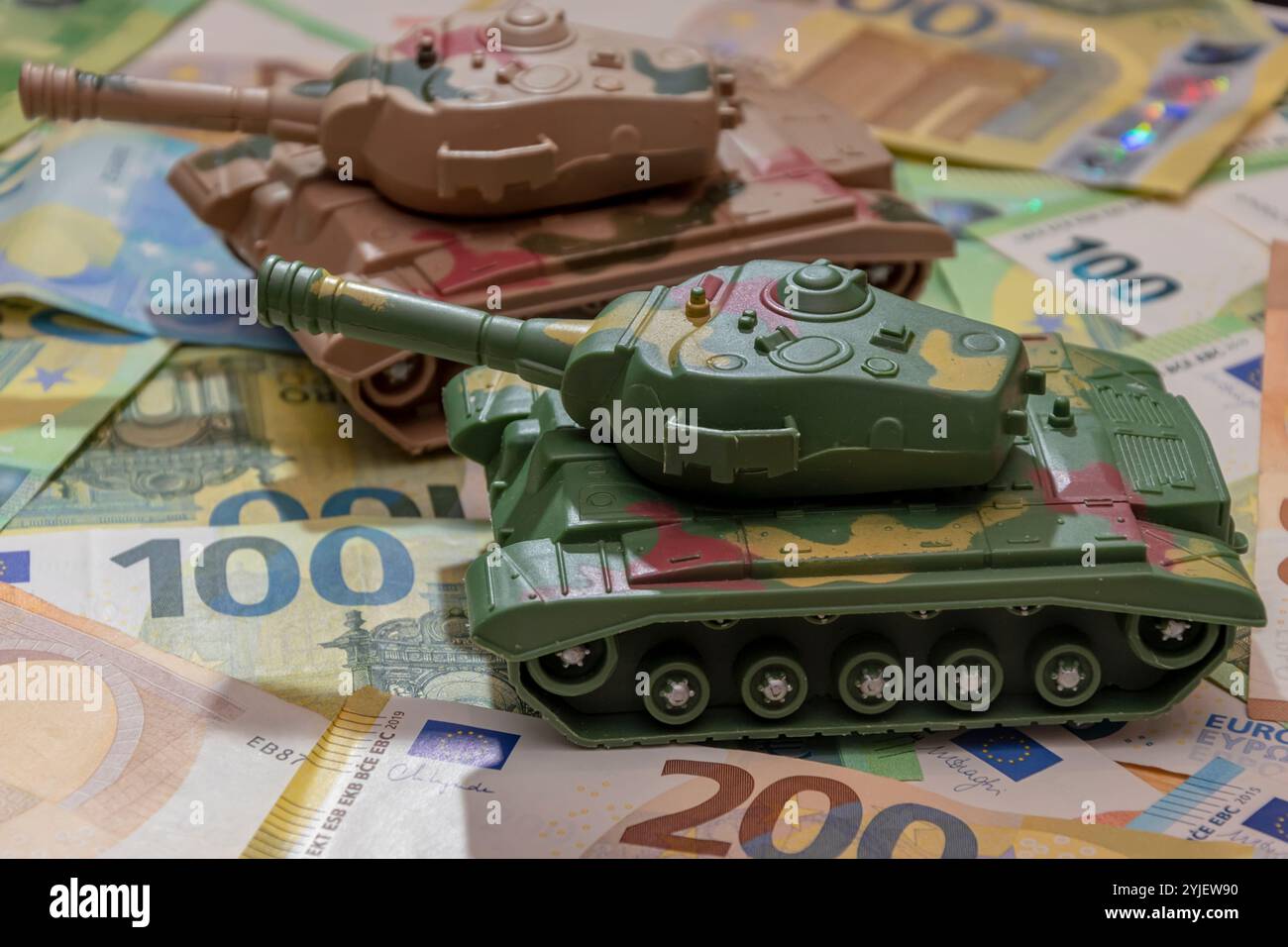 Deux chars militaires jouets, un éparpillement de billets en euros. Concept : dépenses du budget de l'état consacrées à l'armée et aux armes, assistance militaire à l'Ukraine, tr Banque D'Images