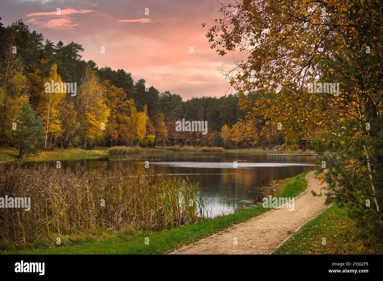 Scène automnale sereine avec un sentier paisible le long d'un lac tranquille entouré d'un feuillage d'automne vibrant, sous un ciel coloré de coucher de soleil Banque D'Images
