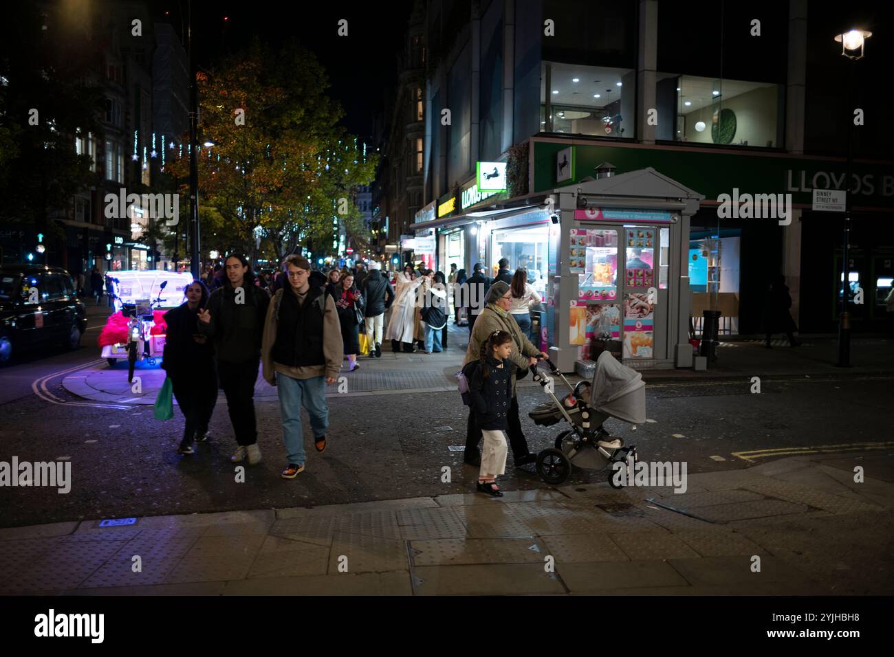 Une femme poussant une poussette avec ses enfants rentre chez elle le long d'Oxford Street par une nuit sombre d'hiver, Angleterre, Royaume-Uni Banque D'Images