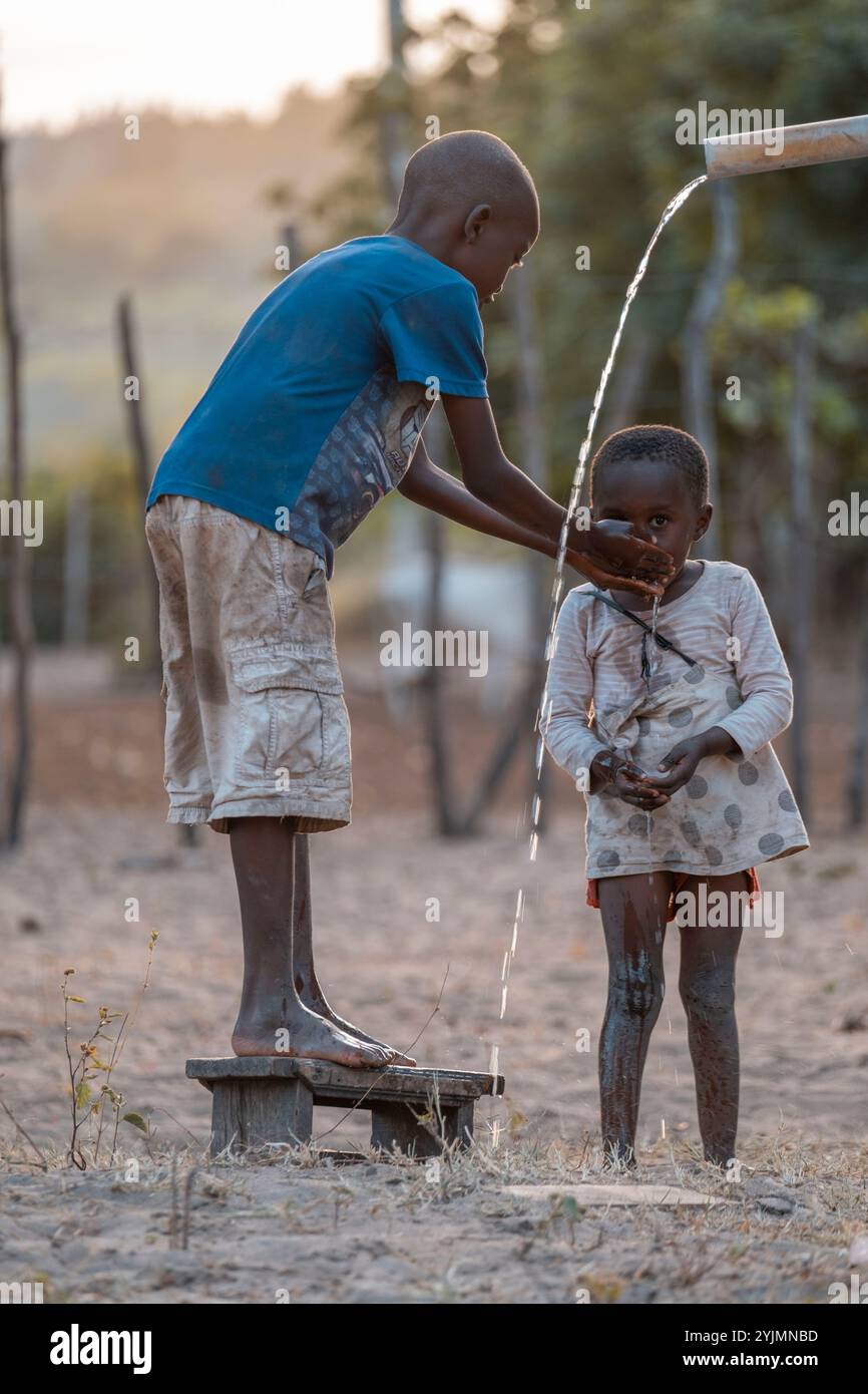 Mali,Kenya - Agoust 20 2021:Un garçon fait boire de l'eau à son frère.Un puits d'eau ou une pompe à eau dans un village en Afrique Banque D'Images