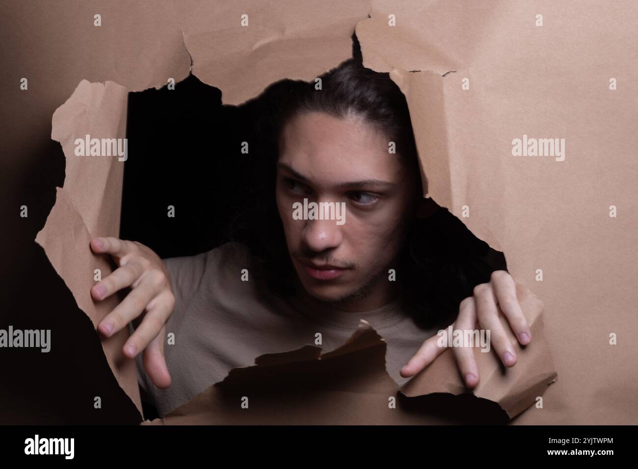 Tête d'homme sortant et regardant à travers un trou de papier avec ses mains poussant le papier de côté. Portrait de studio. Banque D'Images