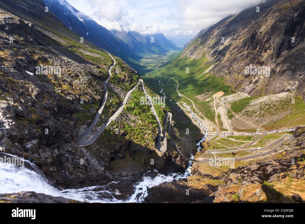 Une vue d'été à couper le souffle sur Trollstigen, Norvège, avec une cascade en cascade au premier plan et une vallée sinueuse qui s'étend au loin. Banque D'Images