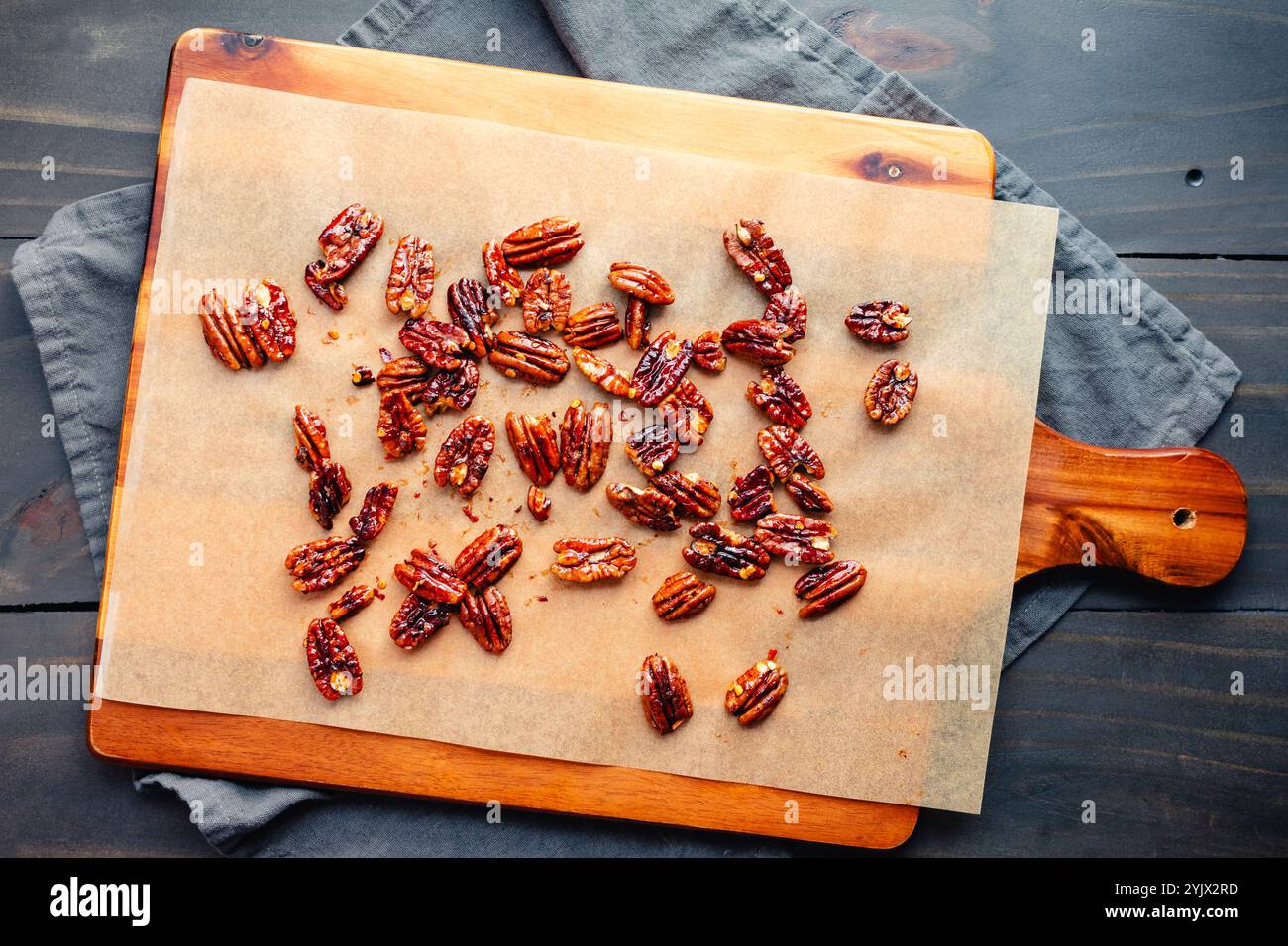 Noix de pécan confites sucrées et épicées sur papier parchemin : noix de pécan grillées sur papier cuisson non blanchi planche à découper en bois doublée Banque D'Images