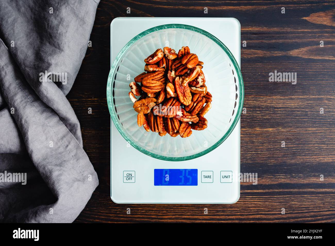 Peser les moitiés de noix de pécan sur une balance de cuisine numérique : vue de dessus des noix dans un bol en verre pesé sur une balance alimentaire sur une table en bois Banque D'Images