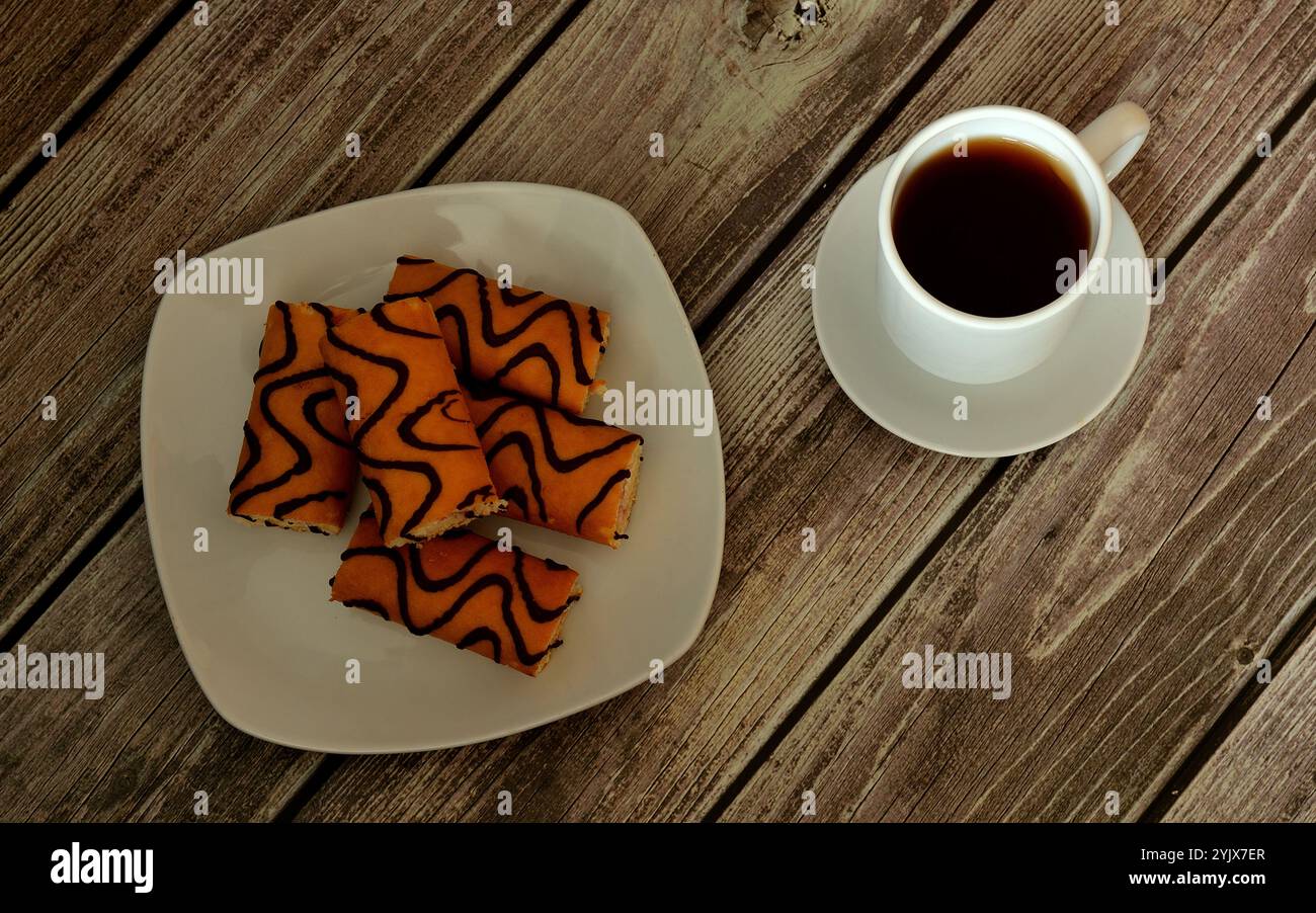 Une assiette avec plusieurs mini petits pains de biscuit en glaçage au chocolat et une tasse de café noir sur une soucoupe avec une cuillère sur une table en bois. Vue de dessus, pose à plat. Banque D'Images