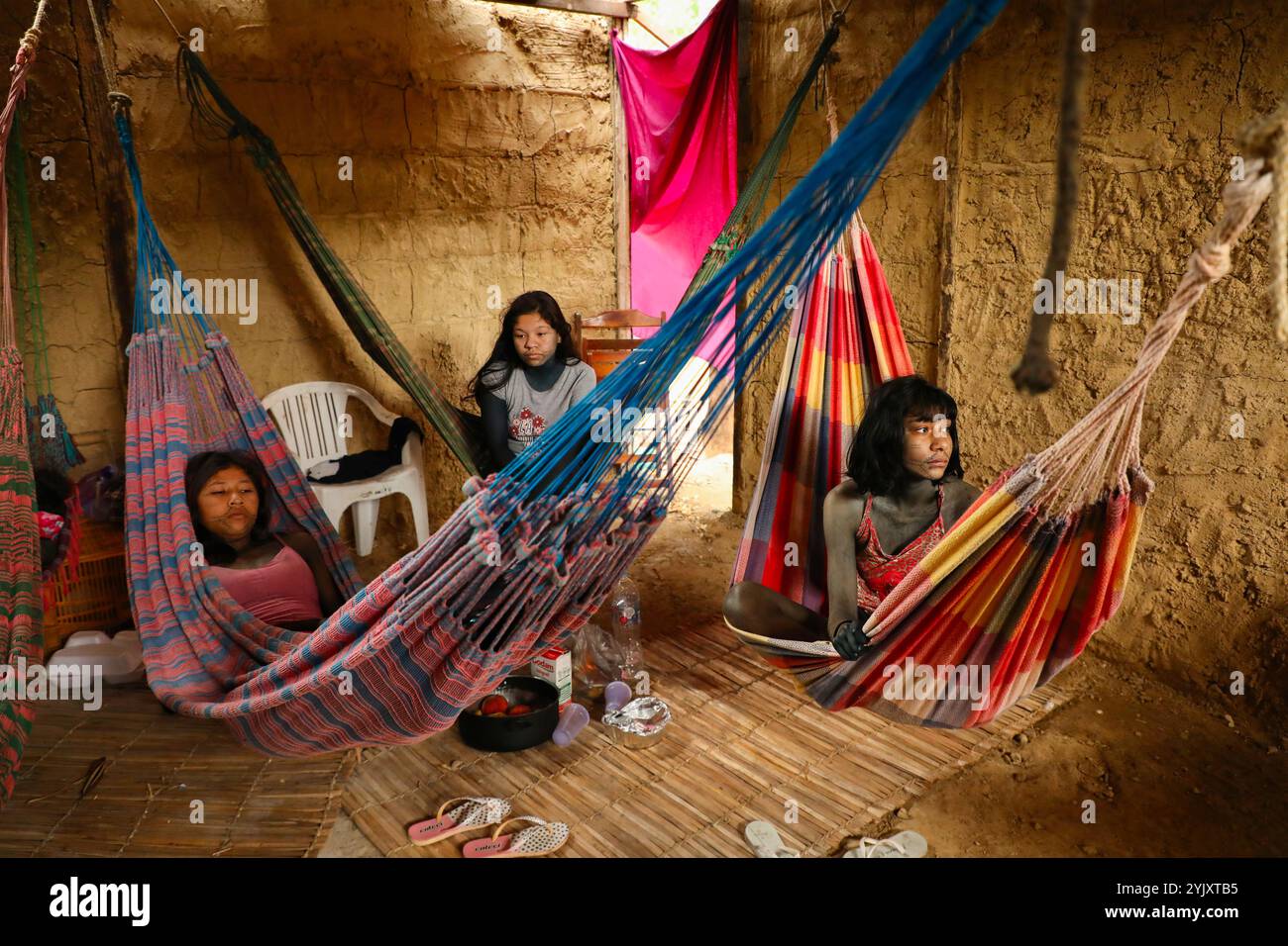 Les jeunes filles qui ont récemment eu leurs règles attendent le début du rituel Wyrau'haw dans une maison de boue dans le village indigène Maracanã de Rio de Janeiro. Parmi les Guajajara, la célébration Wyrau'Haw marque la transition d'une fille vers la féminité pendant ses premières règles. Situé près du stade Maracanã de Rio de Janeiro, le village indigène Maracanã est menacé par des promoteurs immobiliers. Les militants indigènes qui s’y sont installés en 2006 luttent pour protéger cette terre, en maintenant leurs traditions et leur calendrier festif au milieu du paysage urbain. Banque D'Images