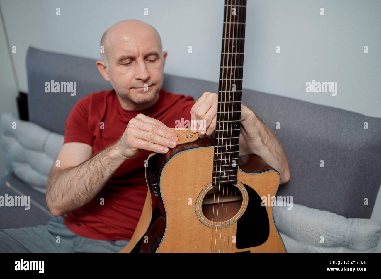 homme mettant une sangle sur une guitare, gros plan à la maison. Détente et assis sur le canapé Banque D'Images