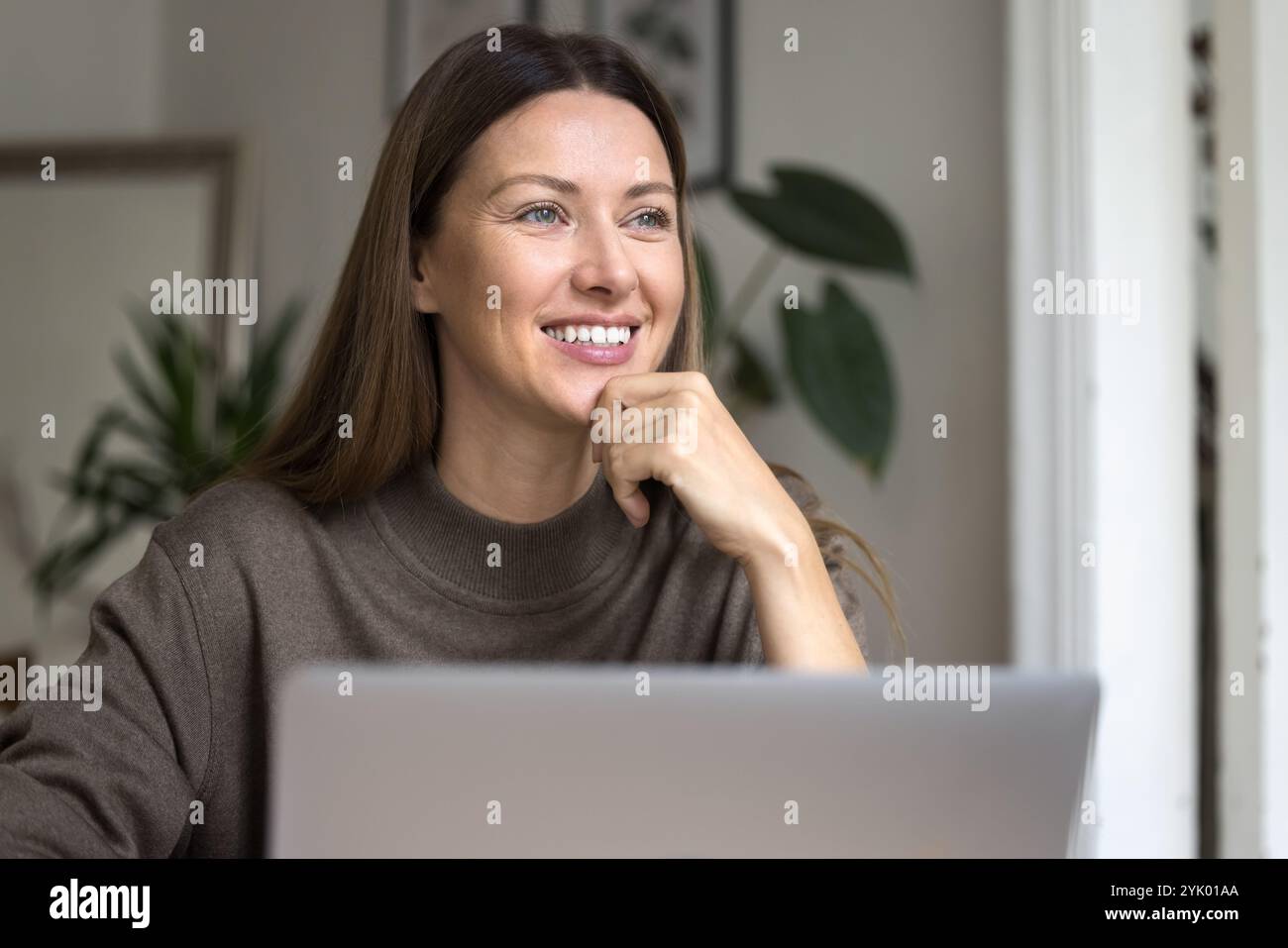 Femme assise devant l'ordinateur portable, regardant loin avec le sourire Banque D'Images