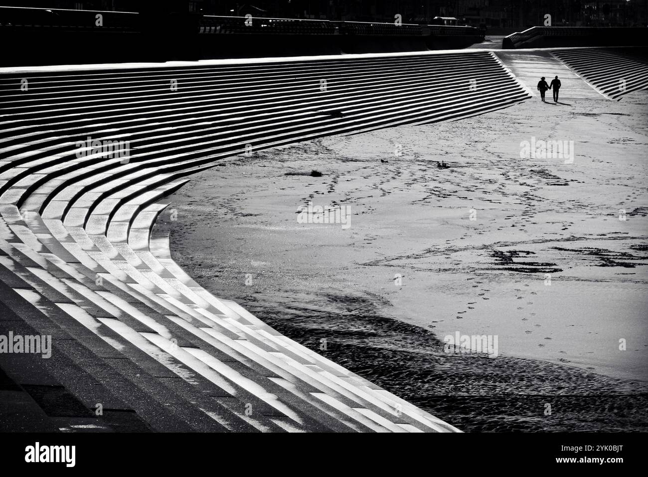 Deux personnes en silhouette marchant sur la plage par des marches sur le mur de mer à Blackpool, Royaume-Uni Banque D'Images