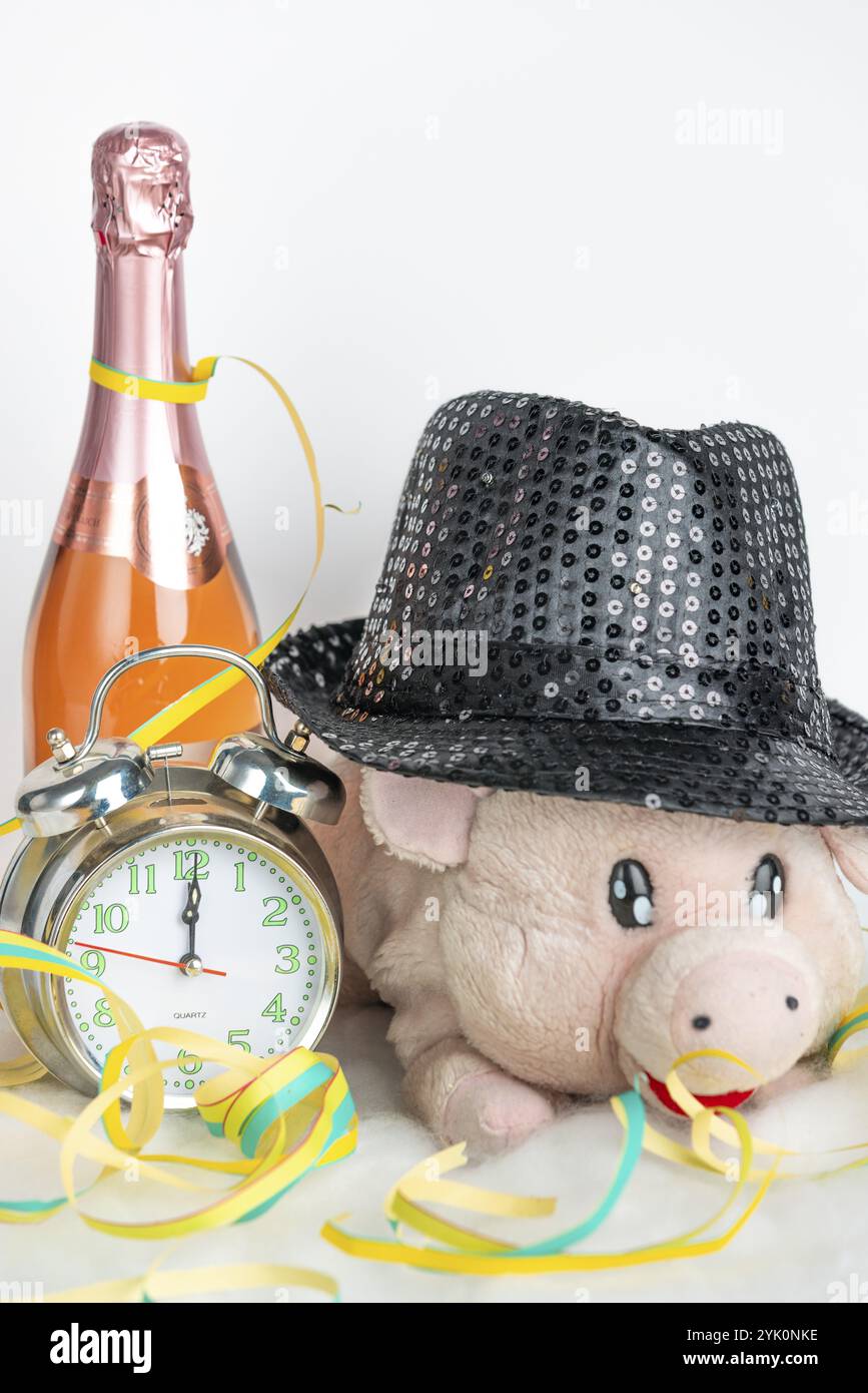 Le cochon en peluche porte un chapeau scintillant, accompagné d'un réveil et d'une bouteille de champagne, la veille du nouvel an Banque D'Images