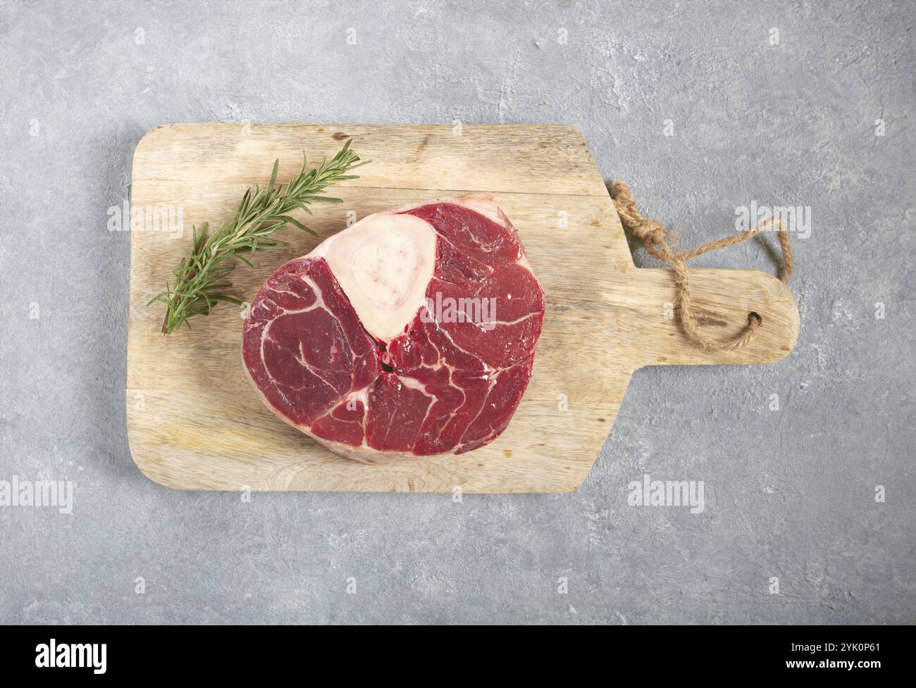 Un jarret sur l'os, viande crue pour ossobuco, sur une planche à découper en bois, avec une branche de romarin, vue de dessus, pas de gens. Banque D'Images