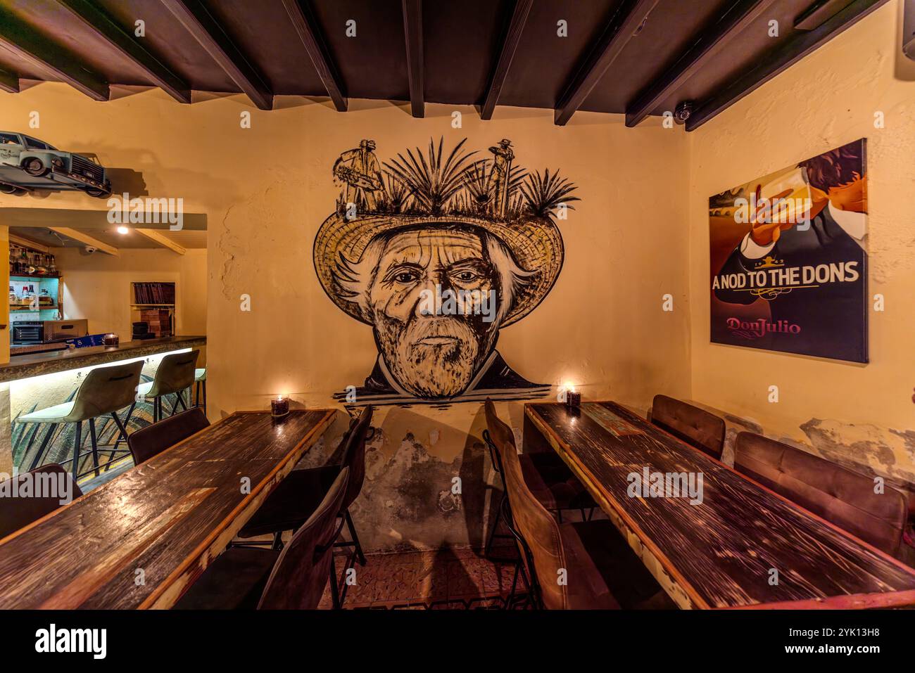 Murale en référence à Don Julio Tequila. Murale dans le MosaCaña Bar & Kitchen sur Penstraat 41, Willemstad, Curaçao, Kòrsou. Le MosaCaña Bar, spécialisé dans le rhum, la tequila, le mescal et Curaçao, intérieur rustique. Une grande murale représentant un homme dans un chapeau de paille, représentant probablement une personne associée à la production d'agave, orne un mur. Le bar dispose d'un mélange de tabourets de bar et de tables, créant une atmosphère détendue. Une affiche encadrée pour Don Julio tequila est également visible. L'ambiance suggère un accent sur les cocktails artisanaux et une célébration des spiritueux mexicains Banque D'Images