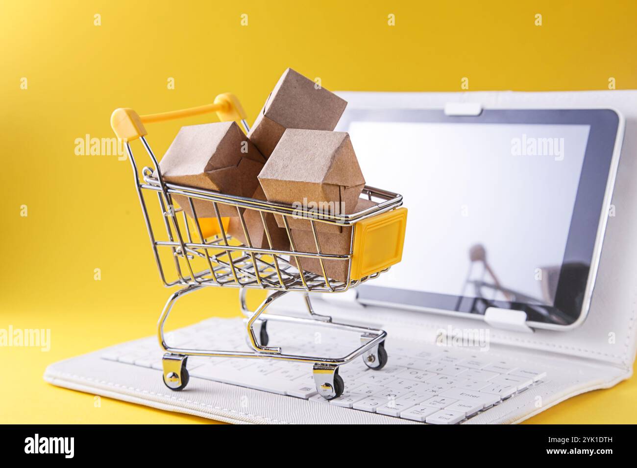 Panier avec boîtes, ordinateur portable blanc sur fond jaune. Internet concept d'achat en ligne. Banque D'Images