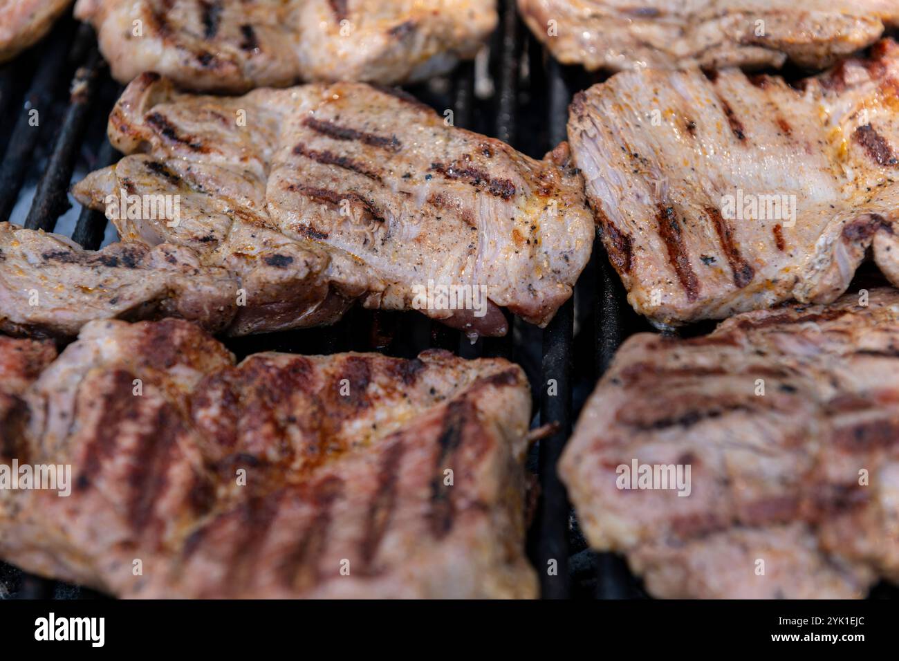 Vue détaillée des steaks de porc cuisant sur un gril, avec des lignes carbonisées et de l'essence fumée, parfait pour le barbecue et les thèmes liés à la nourriture. Banque D'Images