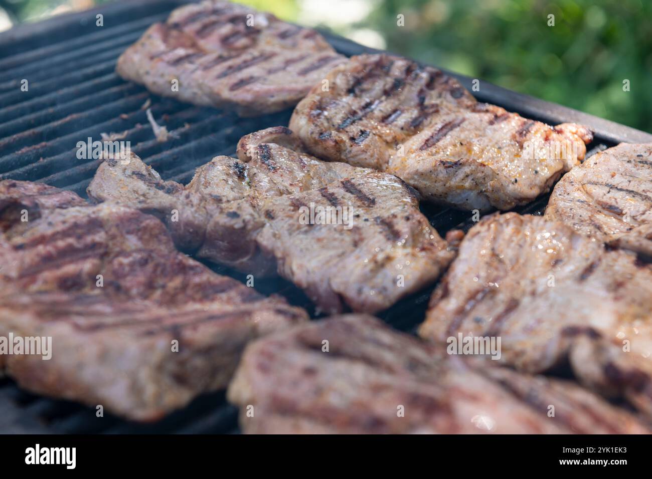 Vue détaillée des steaks de porc cuisant sur un gril, avec des lignes carbonisées et de l'essence fumée, parfait pour le barbecue et les thèmes liés à la nourriture. Banque D'Images