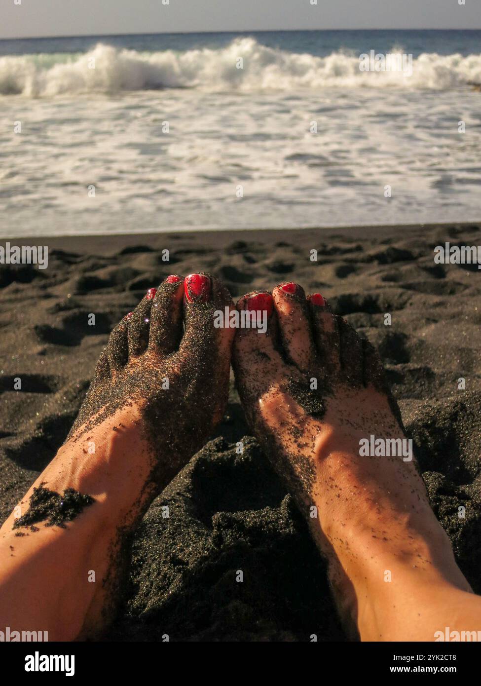 Femme's pieds sur la plage de lave noire avec vernis à ongles rouge sur Gozo / Malte novembre 2015 Banque D'Images