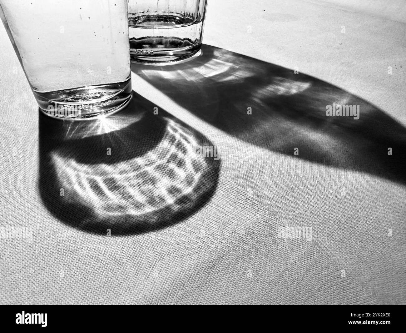 Un verre d'eau et une bouteille d'eau et leurs ombres sur une nappe blanche Banque D'Images