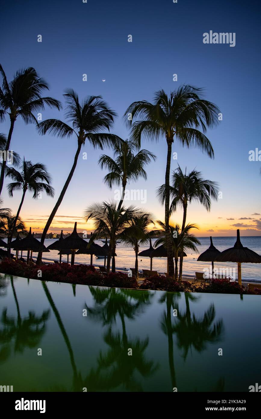 Reflet de cocotiers et de parasols en chaume dans la piscine de Royal Palms Beachcomber Luxury (Beachcomber Resorts) au crépuscule, Grand Baie, R Banque D'Images