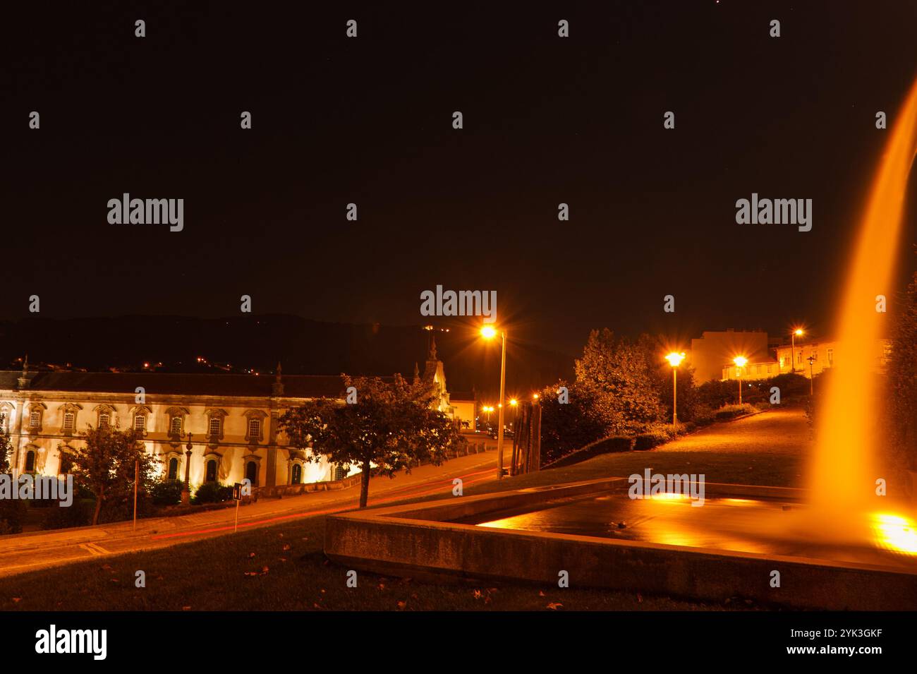 Paysage de nuit d'une fontaine de parc. Paysage nocturne d'une fontaine de parc, d'une route et de quelques bâtiments. Banque D'Images