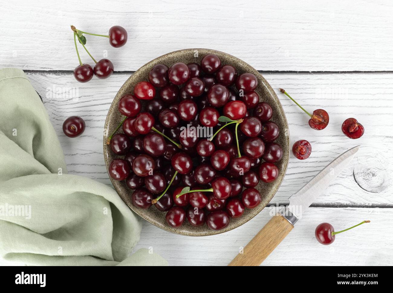 Bol de cerises rouges fraîches et couteau sur fond blanc. Vue de dessus. Banque D'Images