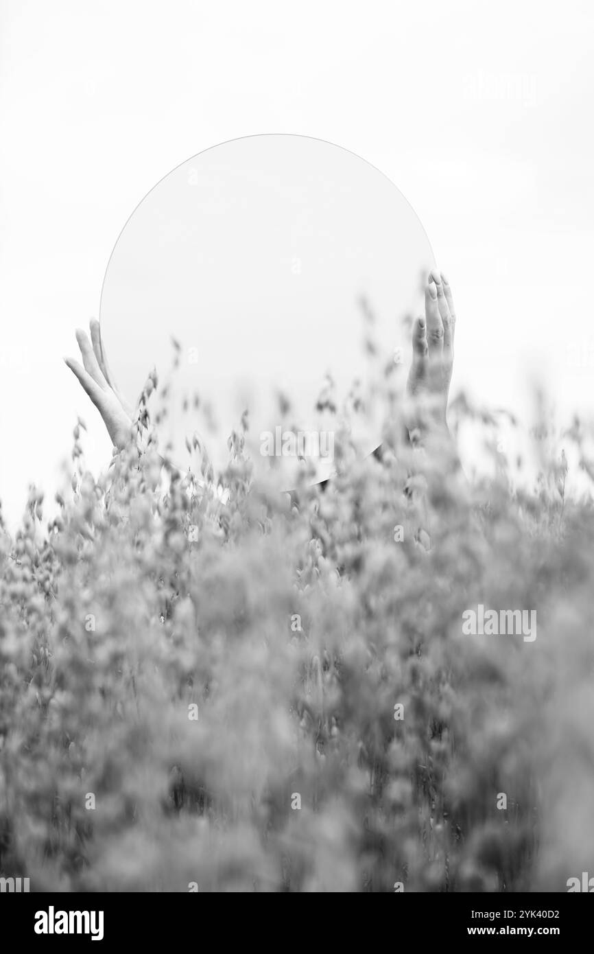 Concept de nature, états d'esprit et concept de mystère. Mains de femme tenant un miroir parmi le blé, reflétant le ciel. L'image contient du bruit et du flou de mouvement Banque D'Images