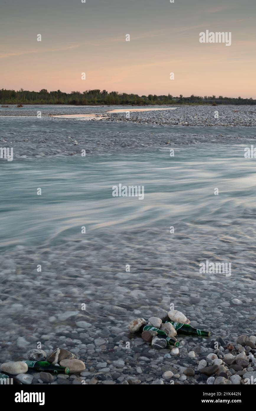 Photo longue exposition de la rivière Tagliamento dans le Frioul au coucher du soleil, avec effet eaux soyeuses et bouteilles de bière entre les rochers et les galets Banque D'Images