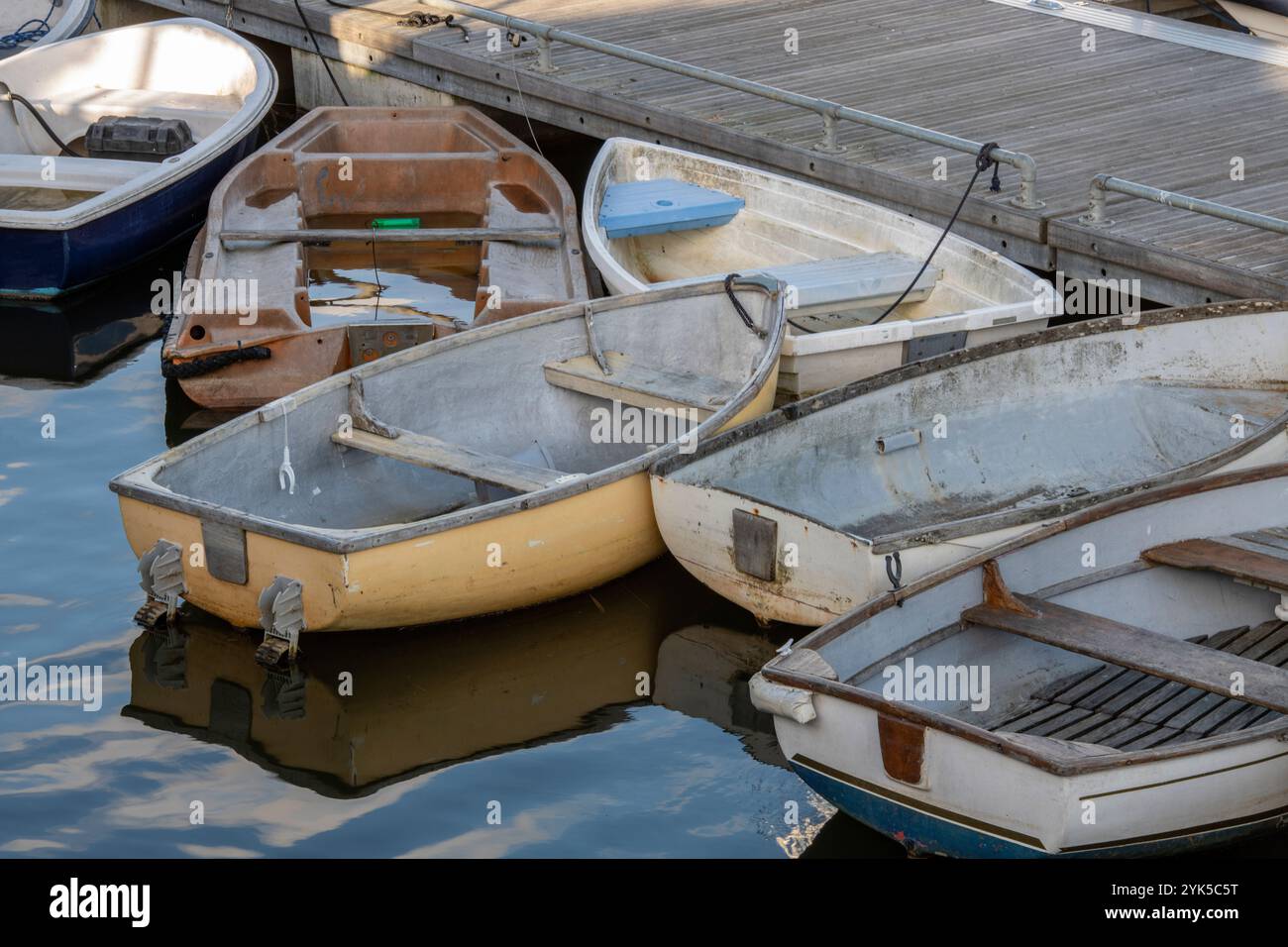 petits bateaux à rames, canots et tenders amarrés ensemble sur un ponton dans une marina de yacht reflétés dans l'eau calme. Canot, tendre et bateau à rames. Banque D'Images