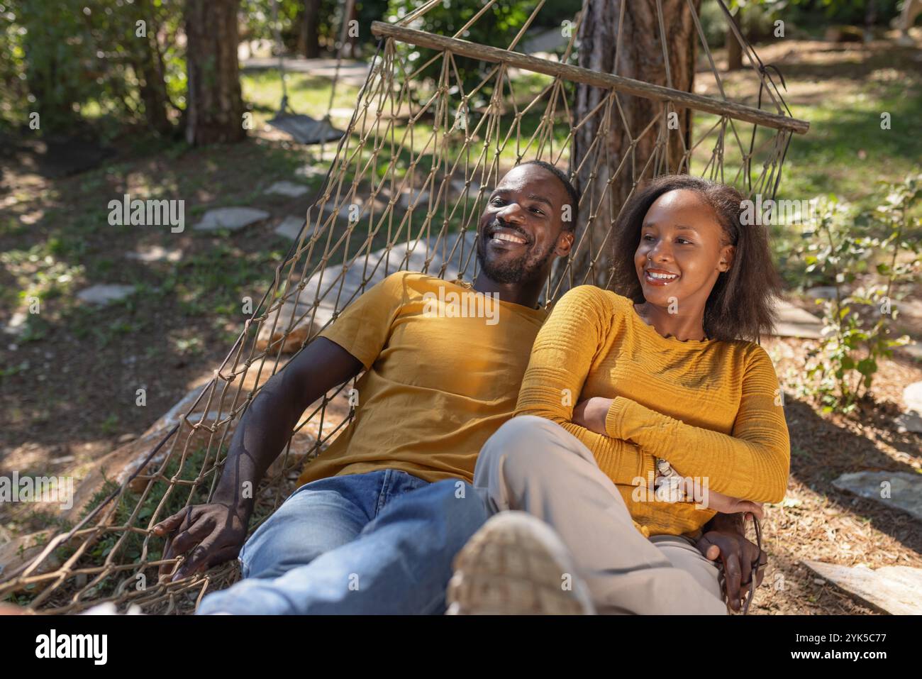 Couple afro-américain souriant insouciant passant leur journée de vacances à se détendre dans un hamac, profitant d'un magnifique environnement naturel de site de glamping. Banque D'Images