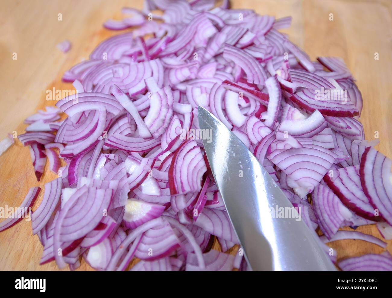 Les oignons rouges frais sont finement tranchés sur une planche à découper en bois, prêts à être cuisinés dans une cuisine familiale confortable. Banque D'Images
