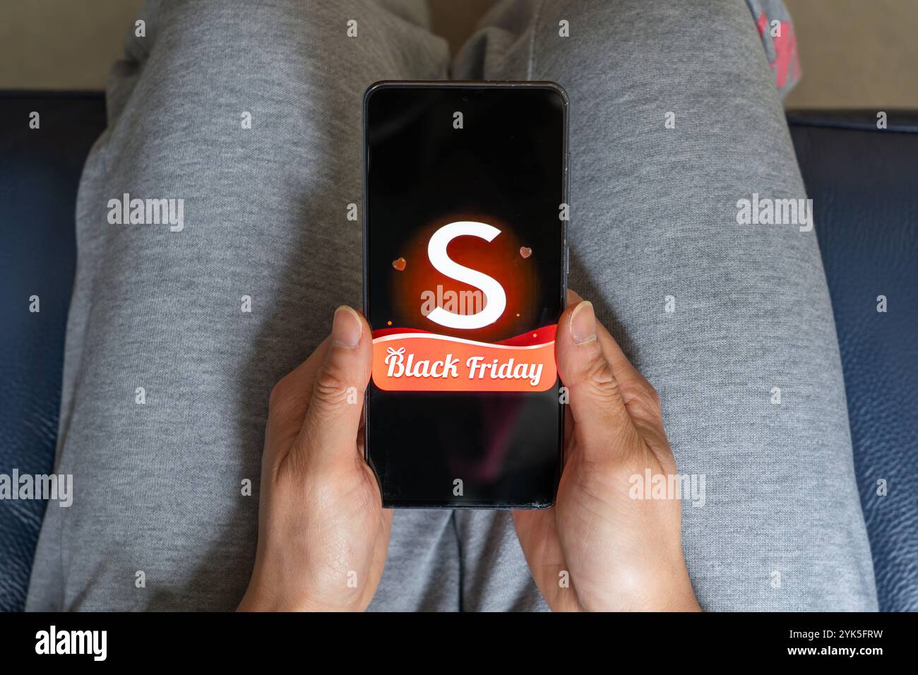 Femme chinoise assise et tenant un smartphone dans ses mains avec le logo Shein et une publicité Black Friday, Royaume-Uni. C'est un détaillant de mode en ligne Banque D'Images