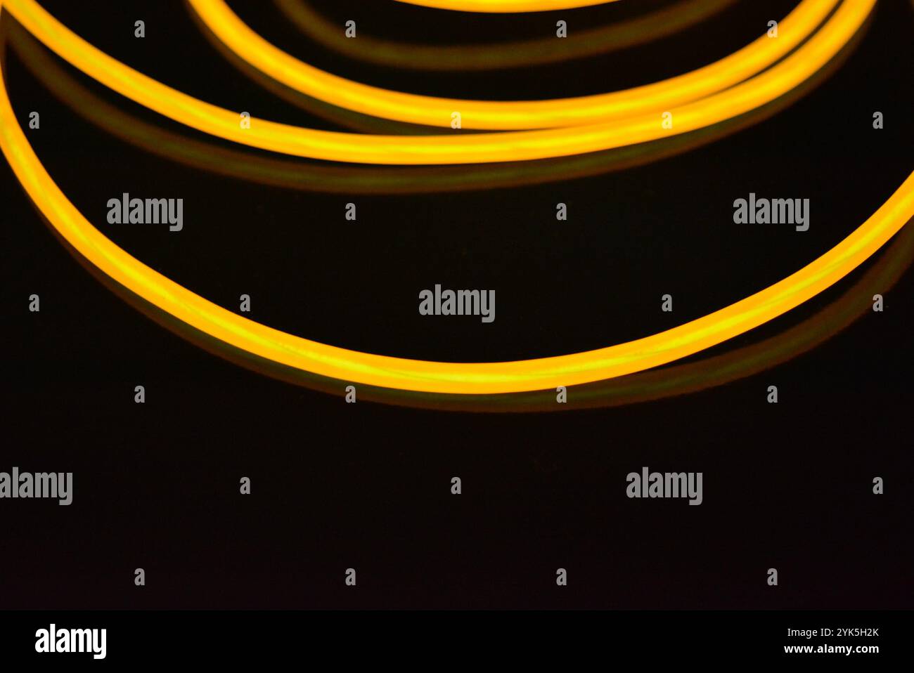 De beaux fils jaunes et orange épais sont chaotiquement situés et tordus sur un fond en plastique noir. Câble électroluminescent, tubes néon. Banque D'Images