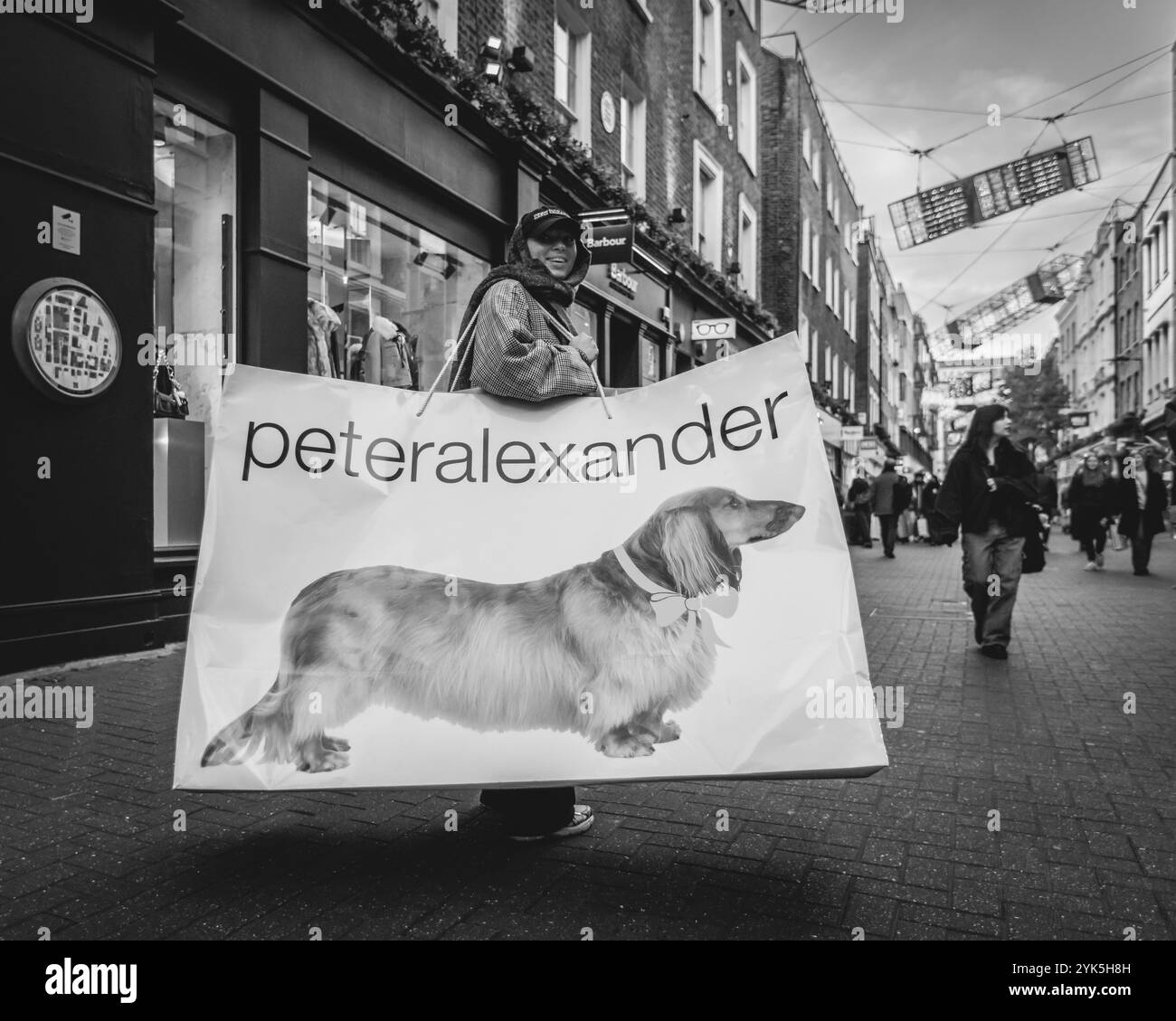 Image en noir et blanc d'un client avec un sac Peter Alexander géant sur la célèbre Carnaby Street à Londres. Banque D'Images