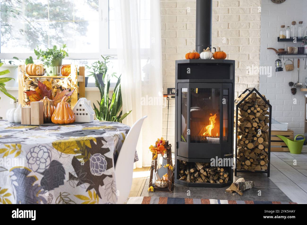 Intérieur ensoleillé lumineux de la maison avec poêle de cheminée en acier en métal noir avec feu et bois de chauffage avec décor d'halloween et ambiance d'automne. Coeur de maison confortable Banque D'Images