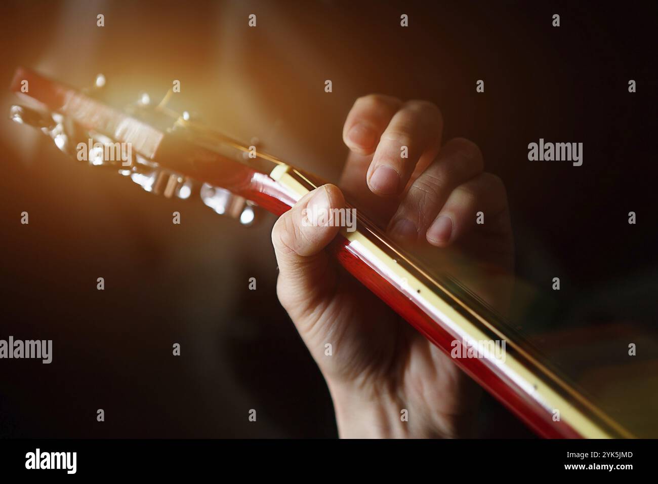 La main d'un homme sur le tableau de bord d'une guitare passe ses doigts à travers les cordes et serre les cordes. Musique instrumentale, leçon de guitare sur la feuille de musique Banque D'Images