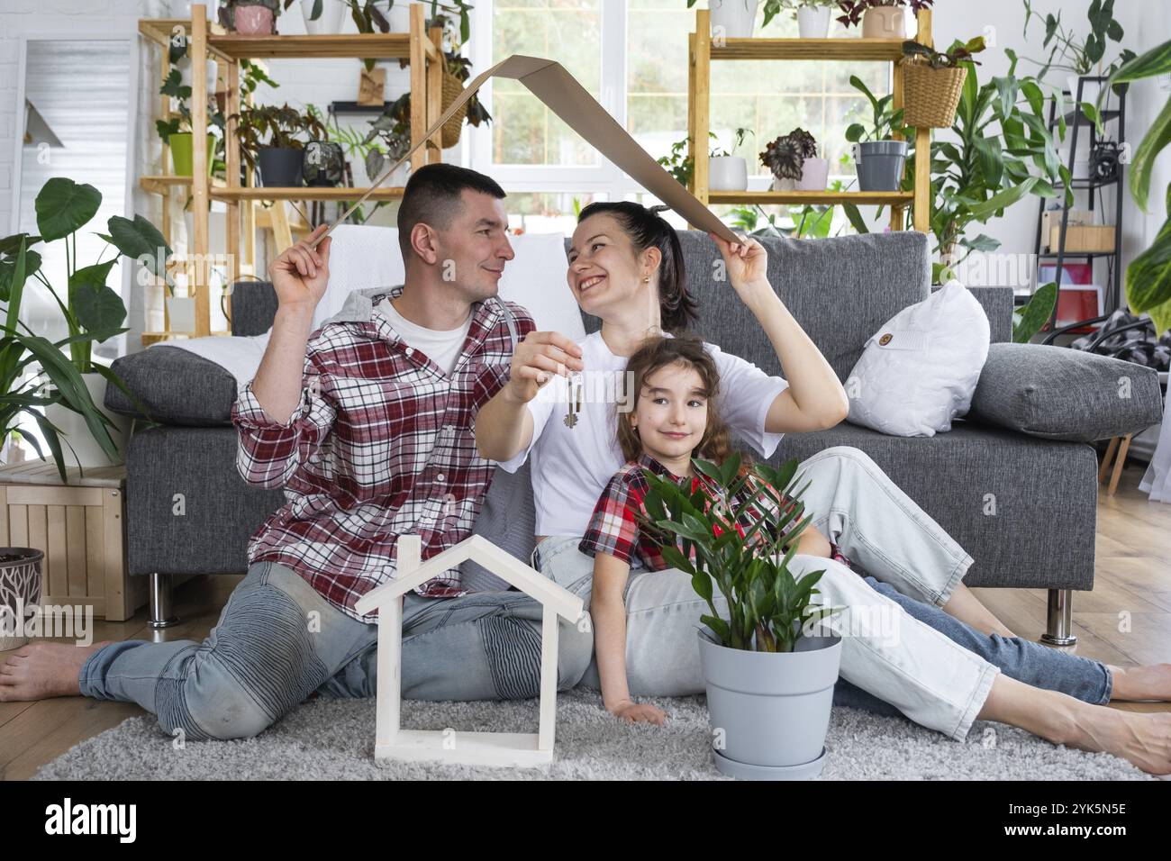 Famille traditionnelle avec enfant apprécient la nouvelle maison, assis sur le canapé et tenant le toit. Hypothèque, assurance et protection, achat et déménagement i Banque D'Images