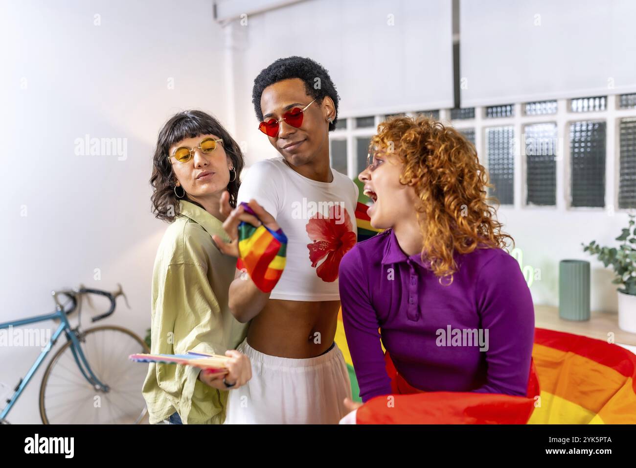 Amis multiethniques et de genre célébrant la diversité et la fierté faisant la fête et dansant à la maison avec le drapeau lgbt Banque D'Images