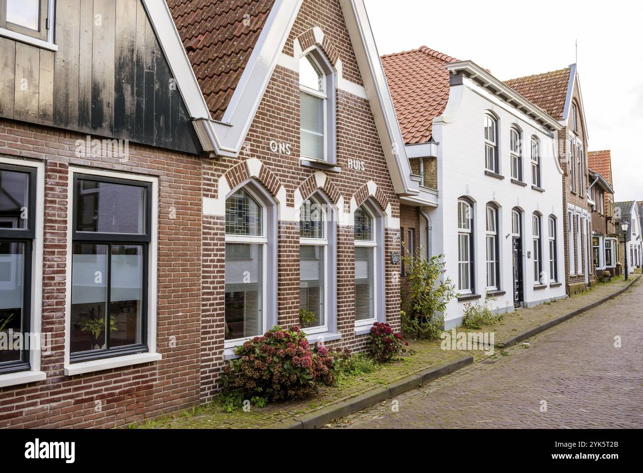 Maisons traditionnelles en briques avec des fenêtres frappantes et des toits rouges le long d'une rue calme du village, Den Hoorn, Texel Banque D'Images