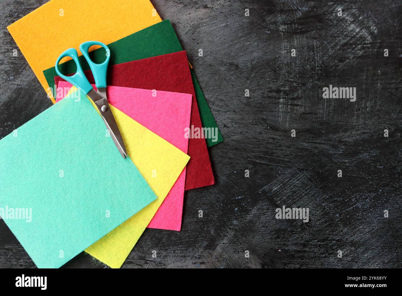 Tissu feutre de différentes couleurs et ciseaux sur fond sombre avec espace de copie. Artisanat et concept de passe-temps. Banque D'Images