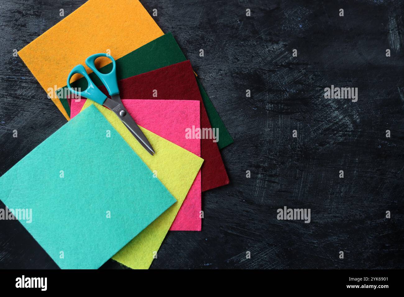 Tissu feutre de différentes couleurs et ciseaux sur fond sombre avec espace de copie. Artisanat et concept de passe-temps. Banque D'Images