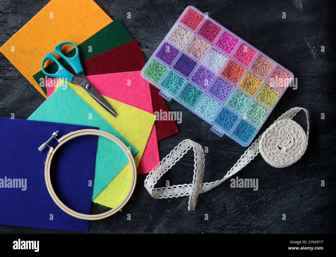 Image colorée des fournitures d'artisanat. Tissu feutre, perles de verre, cerceau de broderie, ciseaux et bande de roulement sur fond sombre. Passe-temps et concept de temps libre. Banque D'Images