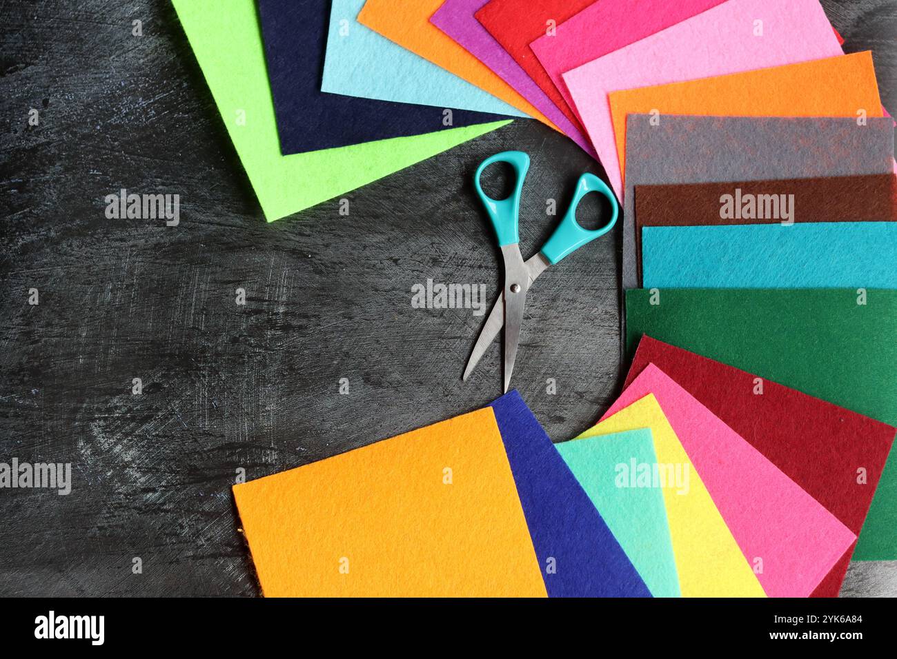 Tissu feutre de différentes couleurs et ciseaux sur fond sombre avec espace de copie. Artisanat et concept de passe-temps. Banque D'Images