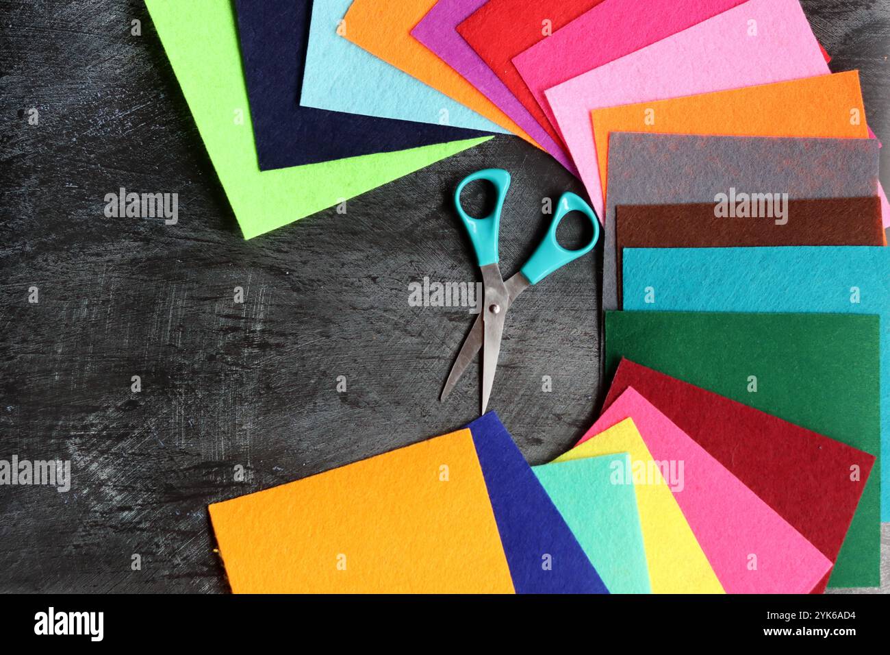 Tissu feutre de différentes couleurs et ciseaux sur fond sombre avec espace de copie. Artisanat et concept de passe-temps. Banque D'Images