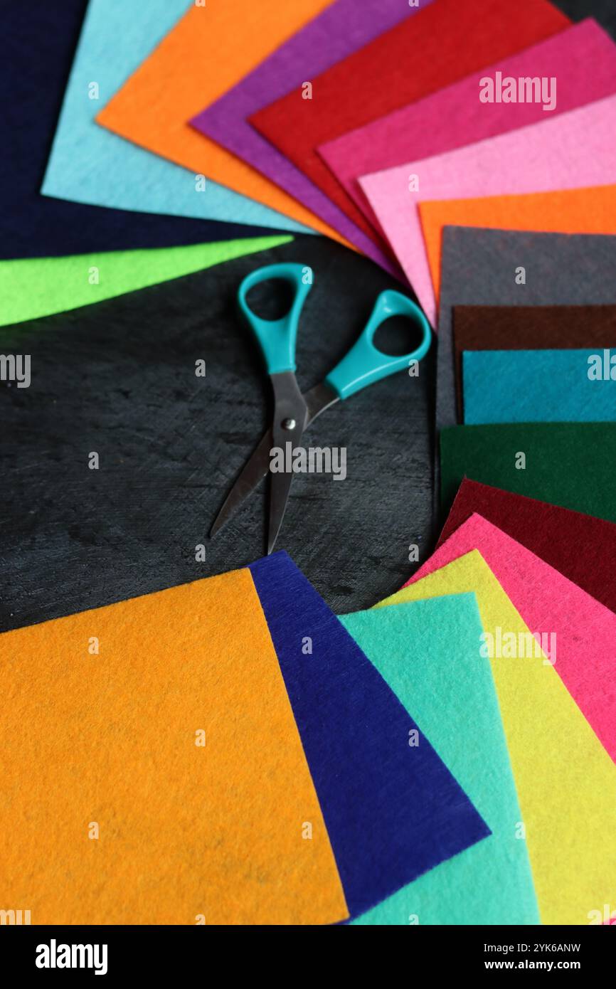 Tissu feutre de différentes couleurs et ciseaux sur fond sombre avec espace de copie. Artisanat et concept de passe-temps. Banque D'Images